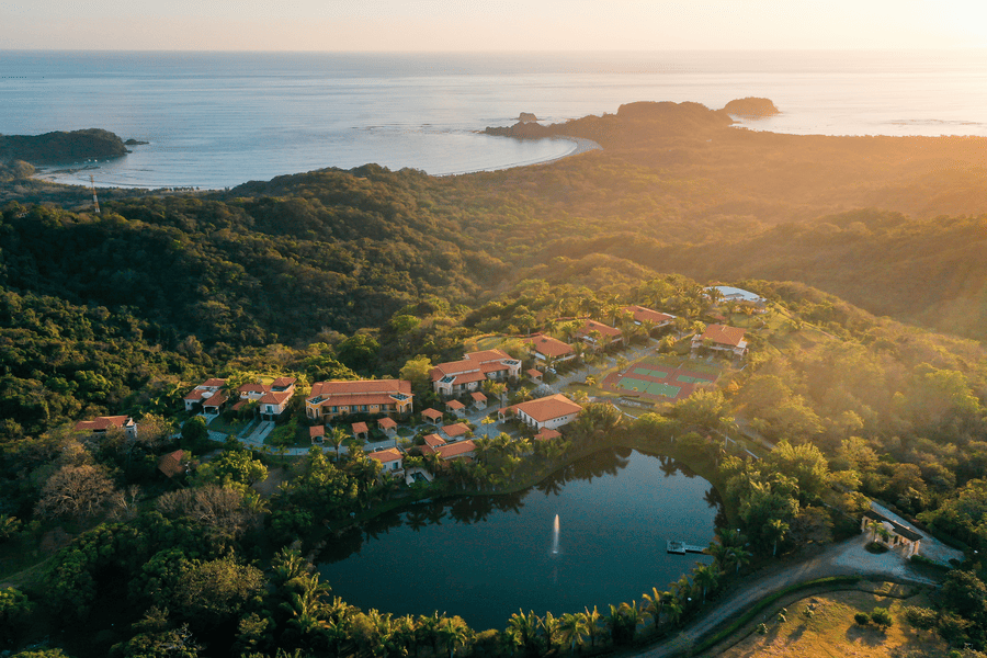 Aerial view of Ventanas del Mar gated luxury community at Playa Carrillo, Costa Rica, showing the community lake and surrounding rainforest at sunset