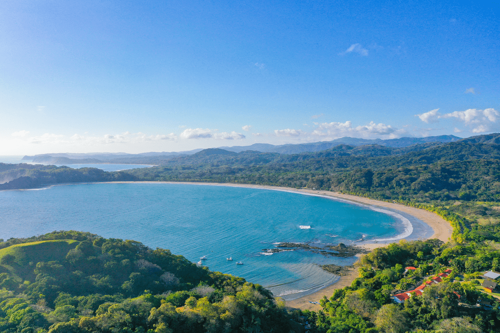 Aerial view of Playa Carrillo in Costa Rica, featuring a crescent-shaped beach, turquoise waters, and lush tropical forest along the Pacific coast.