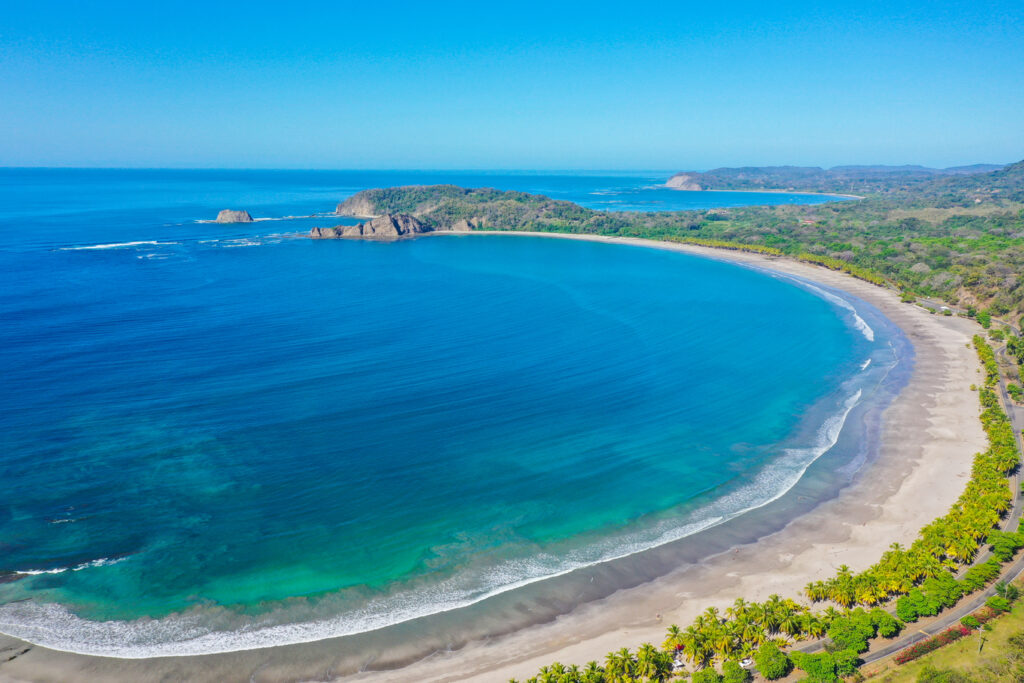 The wide palm-lined crescent of family-friendly Playa Carrillo, Costa Rica, with calm blue water and white sand near Ventanas del Mar