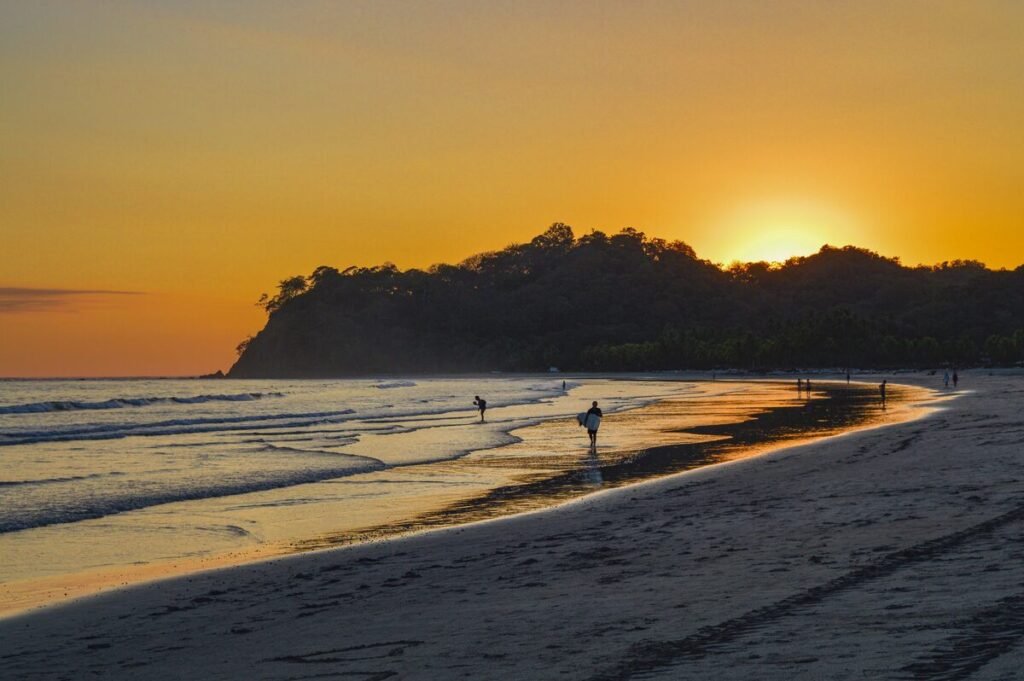 Wide golden family beach at Playa Sámara, Costa Rica, lined with palms and restaurants, with calm reef-protected water for swimming