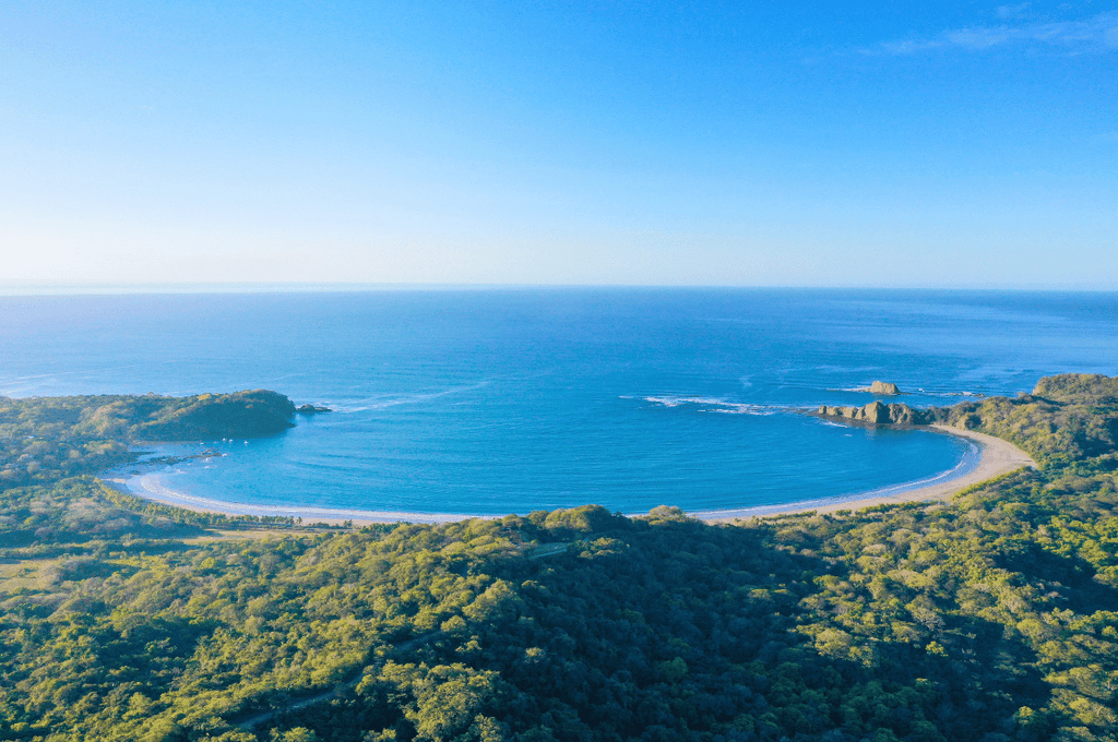 Lush green hills above the calm crescent bay of Playa Carrillo, Costa Rica during green season.