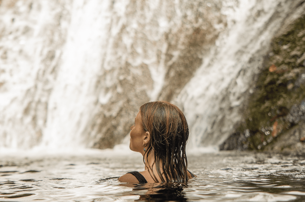 Woman swimming in a natural pool beneath a waterfall during green season near Playa Carrillo, Costa Rica.